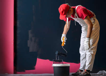 Man painting a wall. Painter in red overall painting wall in black colorの写真素材