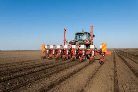 Farmer with tractor seeding crops in the field.