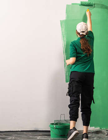 Young women painter in shirt  painting a wall with paint rollerの写真素材