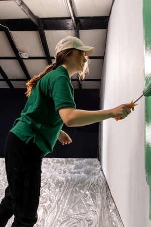 Young women painter in shirt  painting a wall with paint rollerの写真素材