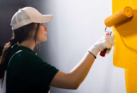 Young women painter in shirt  painting a wall with paint rollerの写真素材