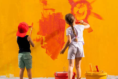 Two kids  holding paintbrushes in their hands and painting  wall in roomの写真素材