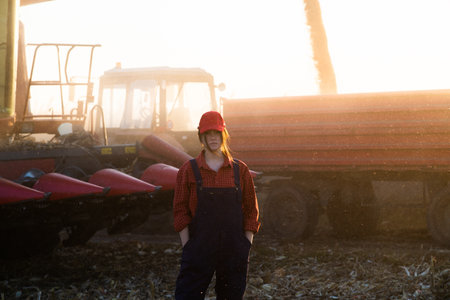 Young farmer girl in the corn field. Agricultural machinery in backgroundの写真素材
