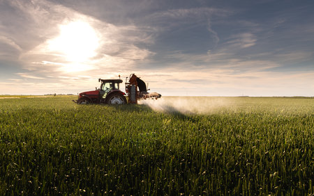 Tractor spraying pesticides over a green fieldの写真素材