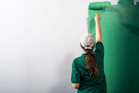 Young women painter in shirt  painting a wall with paint roller