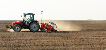 Farmer with tractor seeding crops in the field.