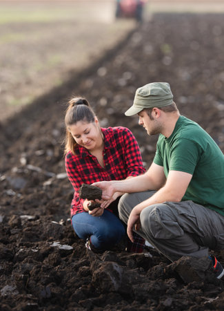 Young farmers examing dirt while tractor is plowing fieldの写真素材