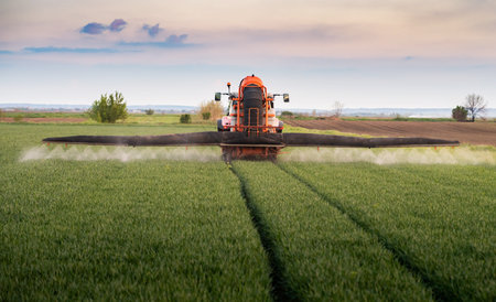 Tractor spraying pesticides over a green fieldの写真素材