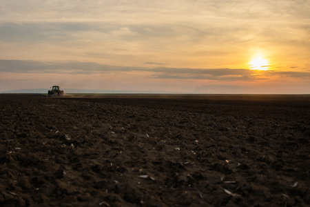 A farmer in a tractor prepares his field as the sun begins to set.の写真素材