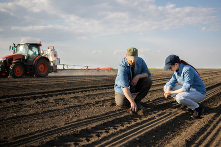 Young farmers examing dirt while tractor is  spraying fieldの写真素材