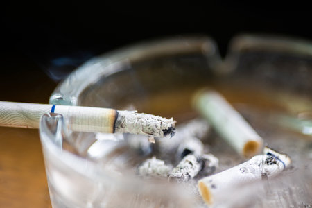 Glass ashtray with lit cigarette on a wooden table
