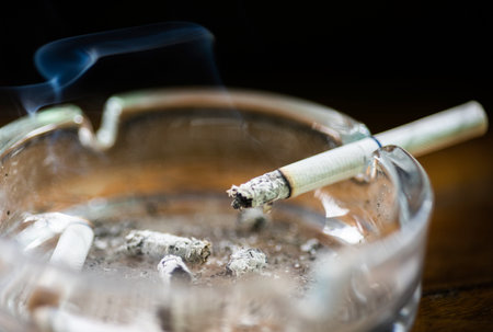 Glass ashtray with lit cigarette on a wooden tableの写真素材