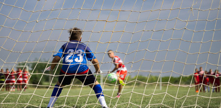 Young Boy Goalkeeper Saving A Football In A Game Of Soccer.