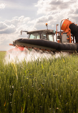 Tractor spraying pesticides over a green fieldの写真素材