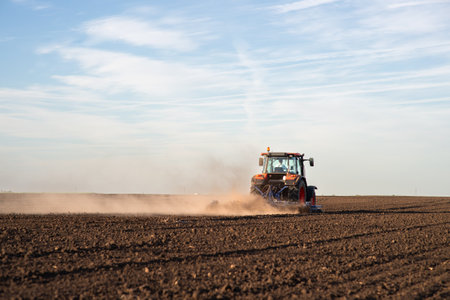 Tractor plowing farm preparing soil for new crop plantation during the evening.