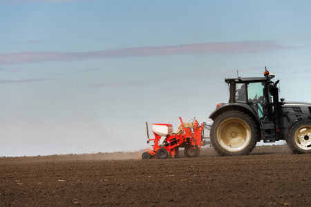 Farmer with tractor seeding crops in the field.