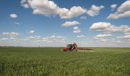 Tractor spraying pesticides over a green field