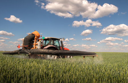 Tractor spraying pesticides over a green field