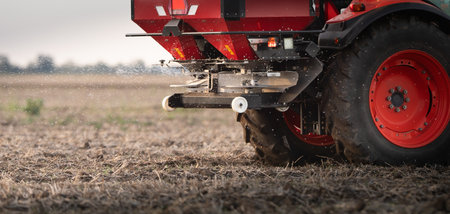 Farmer fertilizing arable land with nitrogen fertilizer in sunset