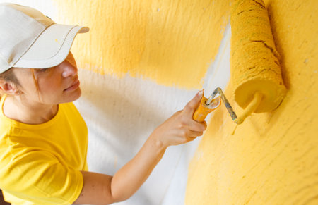 Young women painter in shirt  painting a wall with paint rollerの写真素材
