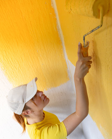 Young women painter in shirt  painting a wall with paint rollerの写真素材