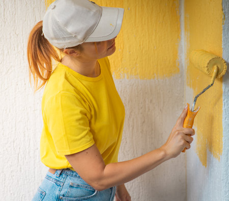 Young women painter in shirt  painting a wall with paint rollerの写真素材
