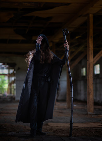 Man in black demon costume with black robe. Silhouette of hooded man.の写真素材