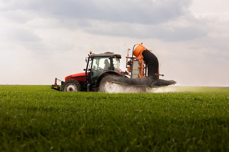 Tractor spraying pesticides over a green field