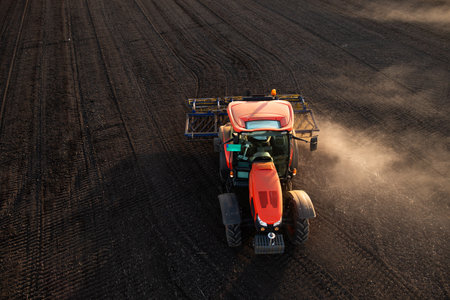 A red tractor prepares the land with a plow. Preparing land for a new crop plantation during sunset