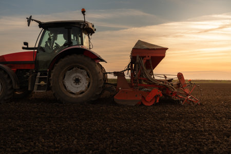 Farmer with tractor seeding - sowing crops at agricultural field. Plants, wheat.