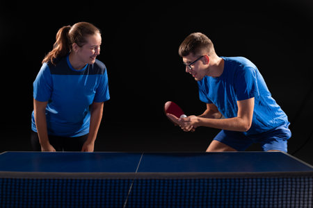 A guy and a girl are playing table tennis together against opponents. Blue table tennis and black backgroundの写真素材