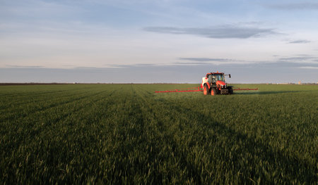 Tractor spraying pesticides over a green fieldの写真素材