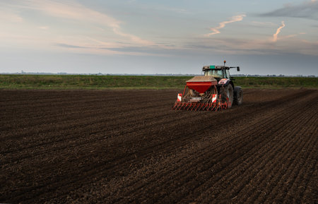 Farmer with tractor seeding - sowing crops at agricultural fields in springの写真素材