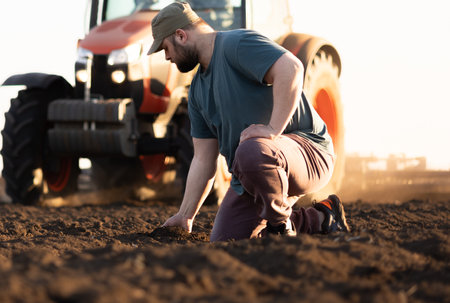 Satisfied tractor driver after work on agricultural field stands next to tractor. Farming and harvestingの写真素材