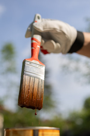 Close-up of a dipping brush into a bucket full of brown paint. Impregnating boards. Varnish finish coating. Manual work.の写真素材