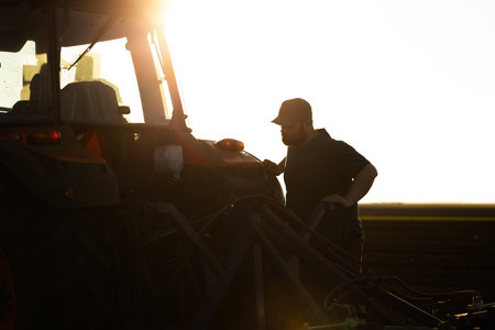 Satisfied tractor driver after work on agricultural field stands next to tractor. Farming and...