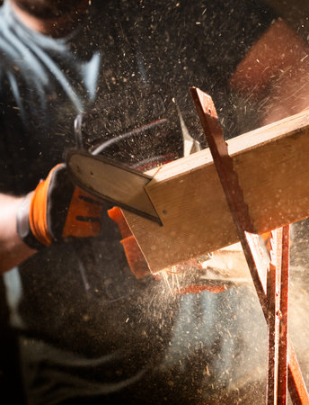 Experienced builder cuts a beam in two pieces with a chainsaw.