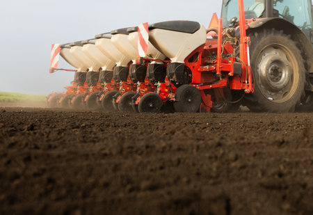 Farmer with tractor seeding - sowing crops at agricultural field. Plants, wheat.