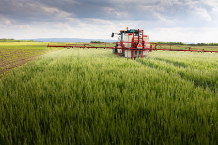 Tractor spraying pesticides over a green field