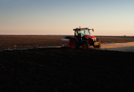 Tractor on the field during sunset. Tractor plows the field in the evening at sunsetの写真素材