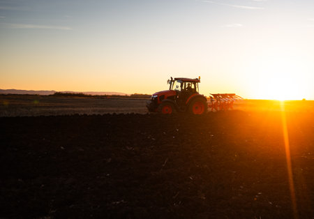 Tractor on the field during sunset. Tractor plows the field in the evening at sunsetの写真素材