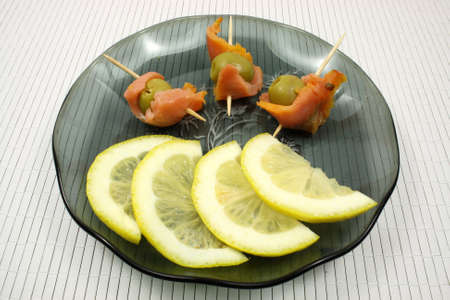Slices of a smoked humpback salmon with olives and a lemonの写真素材
