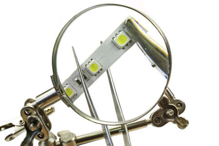 LED tape and tweezers through magnifying glass on a white background