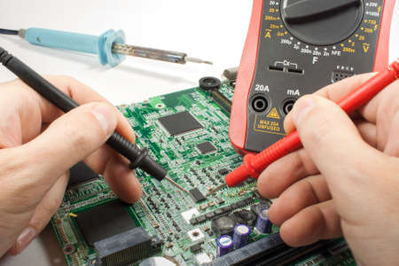 Digital multimeter with probe and soldering iron in the engineer's hands in a workshop