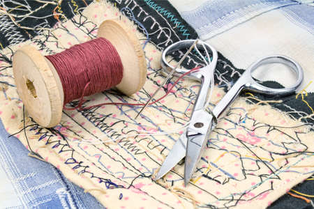 Miniature scissors and a wooden spool of thread at the working place of the tailor
