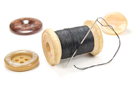 Vintage wooden spool of black thread, needle and buttons on white background