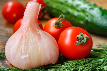 Cherry tomatoes, pink pickled garlic, cucumber and fresh dill on a old wooden tableの写真素材