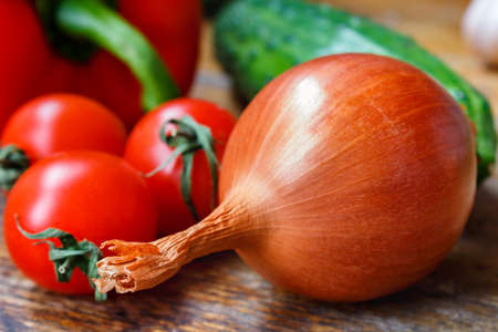 Large onion, cherry tomatoes, sweet peppers and cucumbers on a old wooden tableの写真素材