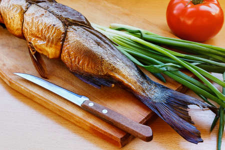 Smoked fish on a wooden cutting board with green onions and tomatoの写真素材