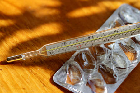 Mercury thermometer and empty blister pack from tablets on a wooden tableの写真素材